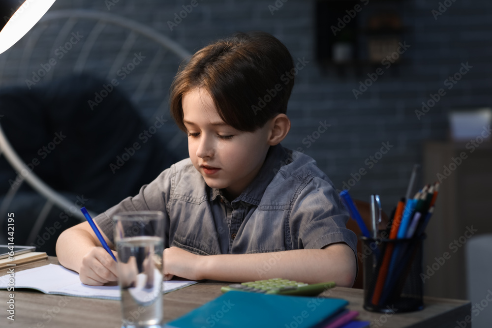 Little boy doing his homework at home late in evening