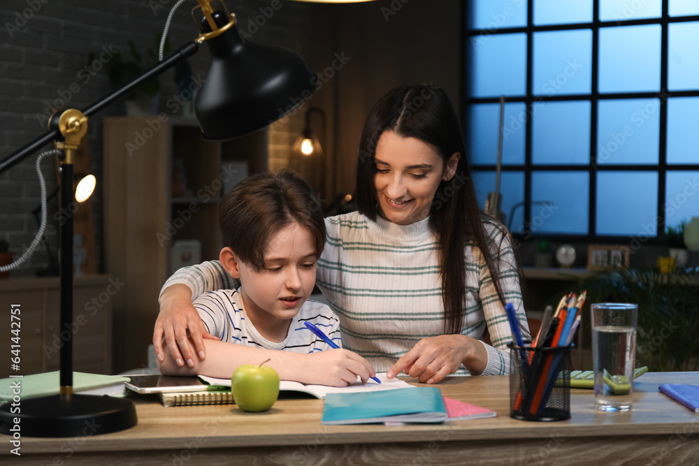 Little boy and his mother doing homework at home late in evening