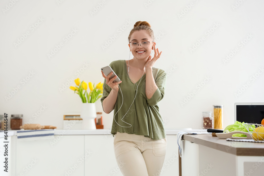 Happy young woman listening to music and dancing in light kitchen