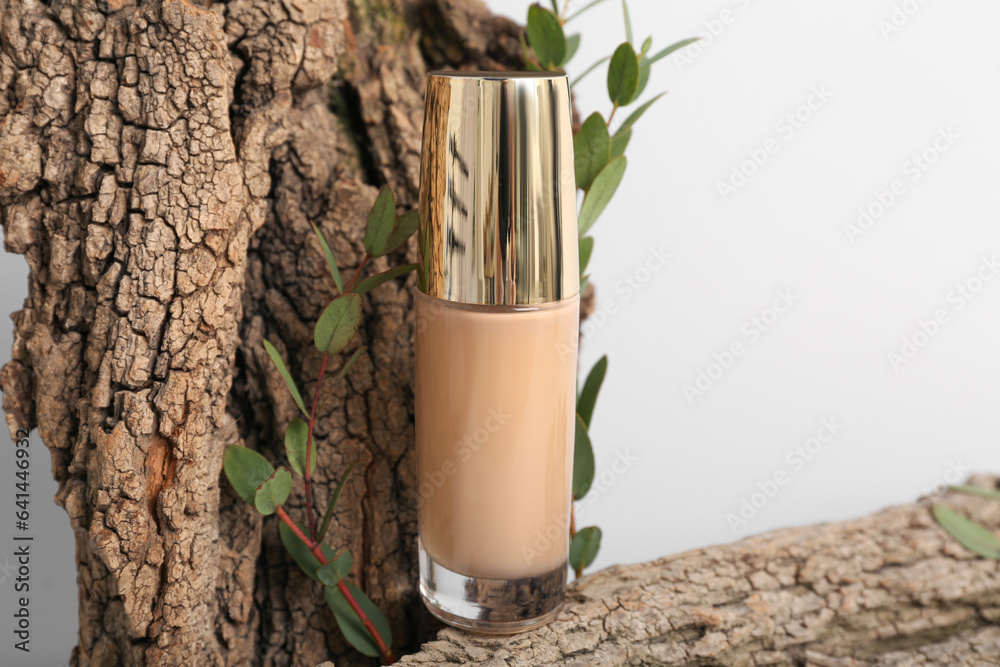 Bottle of makeup foundation, tree bark and eucalyptus branches on light background, closeup