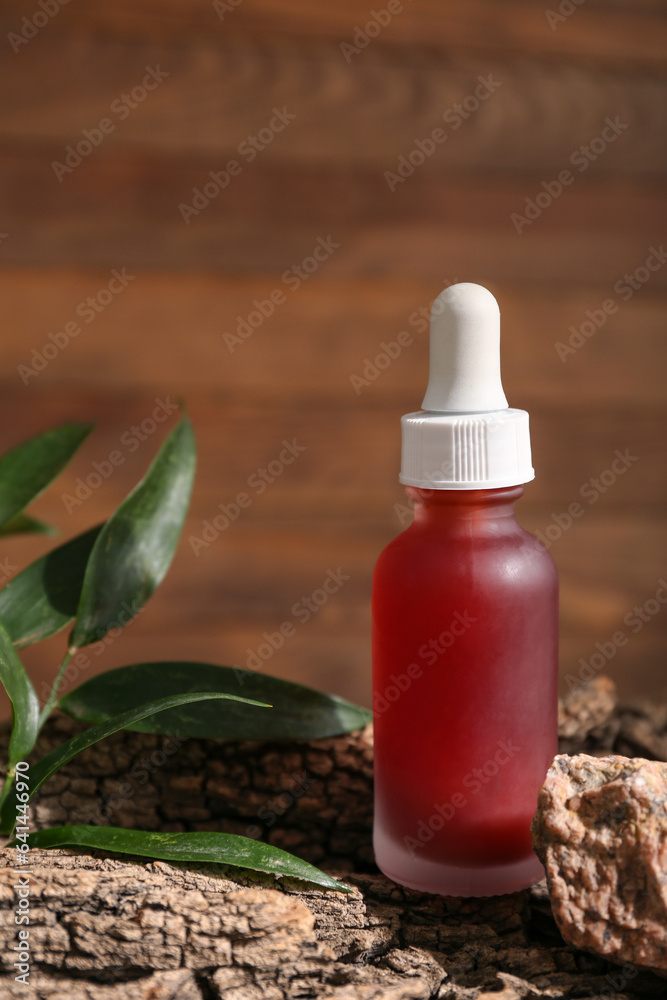 Bottle of essential oil, tree bark and plant leaves on wooden background, closeup