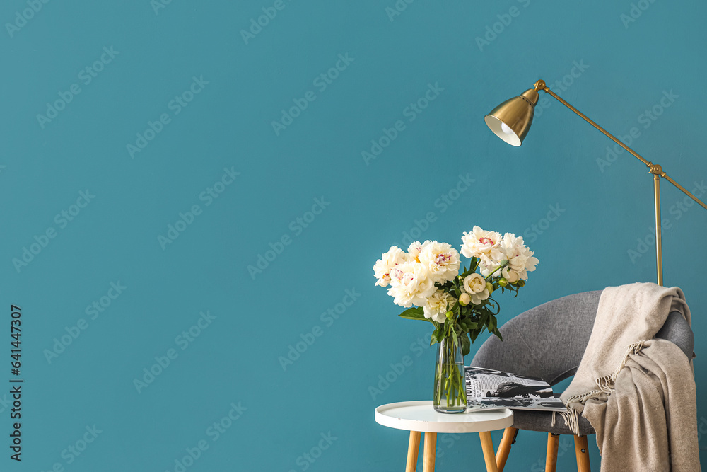 Vase of white peonies with coffee table, chair and floor lamp near blue wall