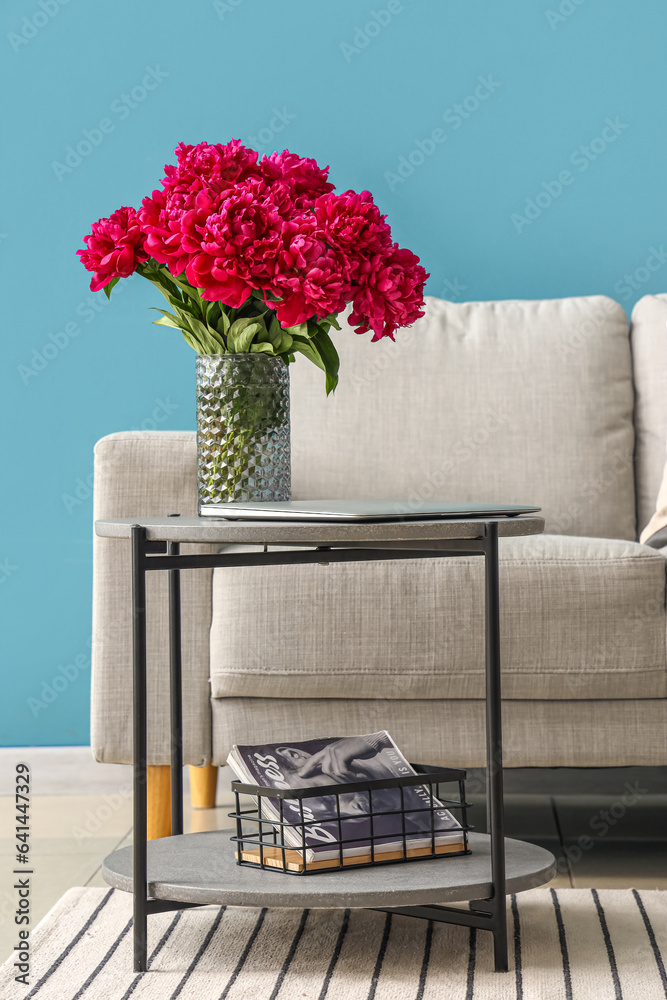 Vase of red peonies with coffee table and couch near blue wall