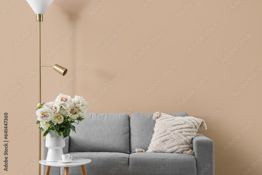 Vase of white peonies with table, couch and floor lamp near beige wall