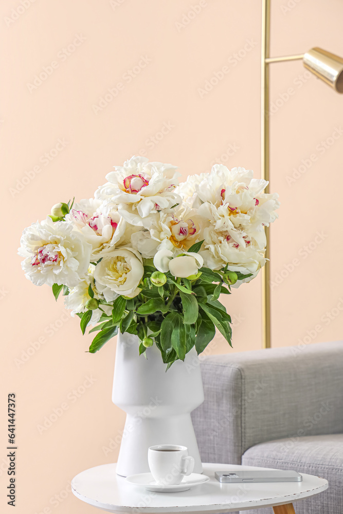 Vase of white peonies with coffee table, couch and floor lamp near beige wall