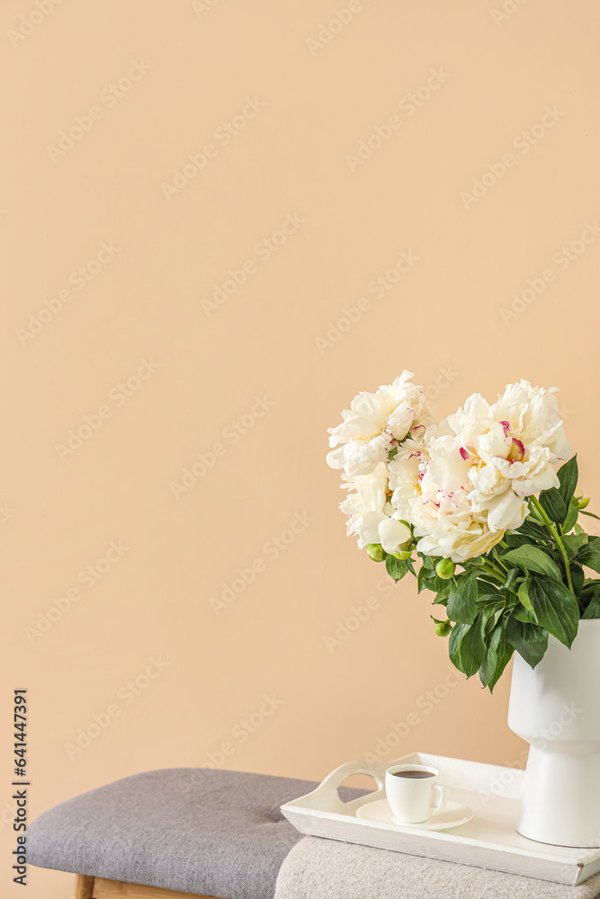 Vase of white peonies with cup of coffee on tray near beige wall