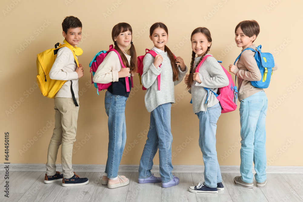 Little pupils with backpacks near beige wall