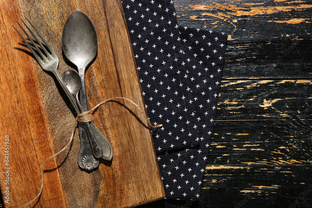 New cutting board, spoons and fork on black wooden background