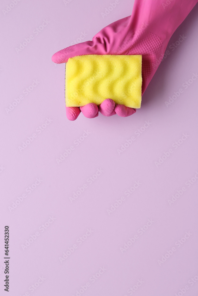 Hand in rubber glove holding yellow sponge on lilac background