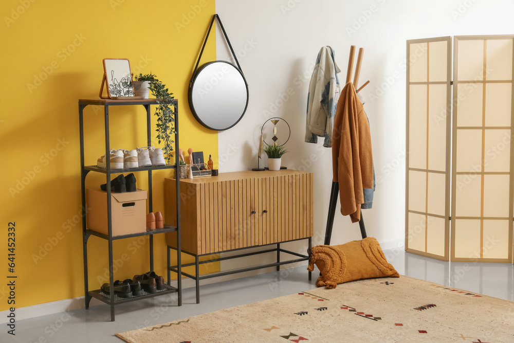 Interior of stylish hallway with mirror, wooden cabinet, shoe stand and rack