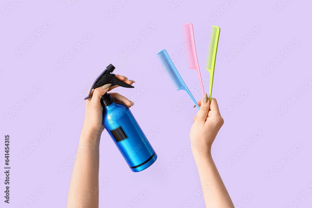 Female hands with hair spray and different combs on lilac background