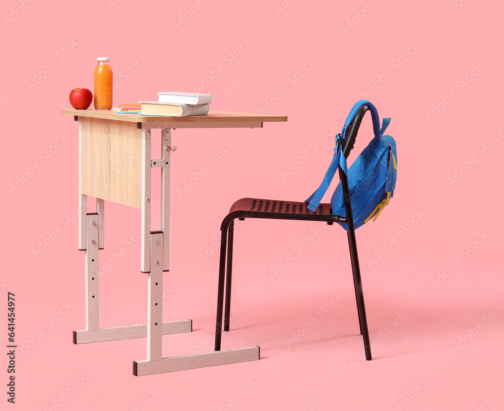 Modern school desk with backpack and stationery on pink background