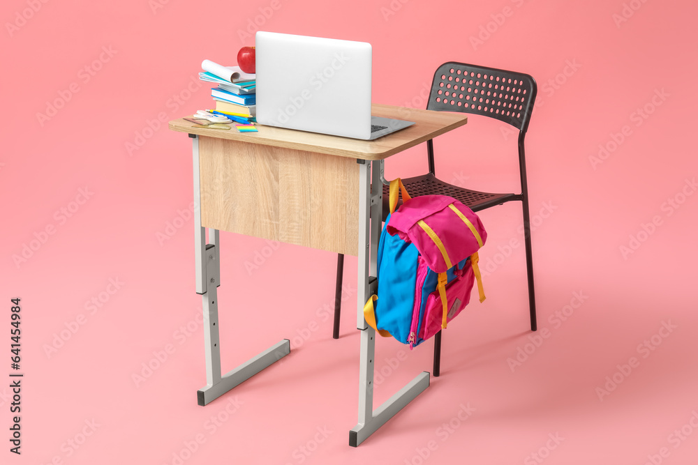 Modern school desk with backpack, laptop and stationery on pink background