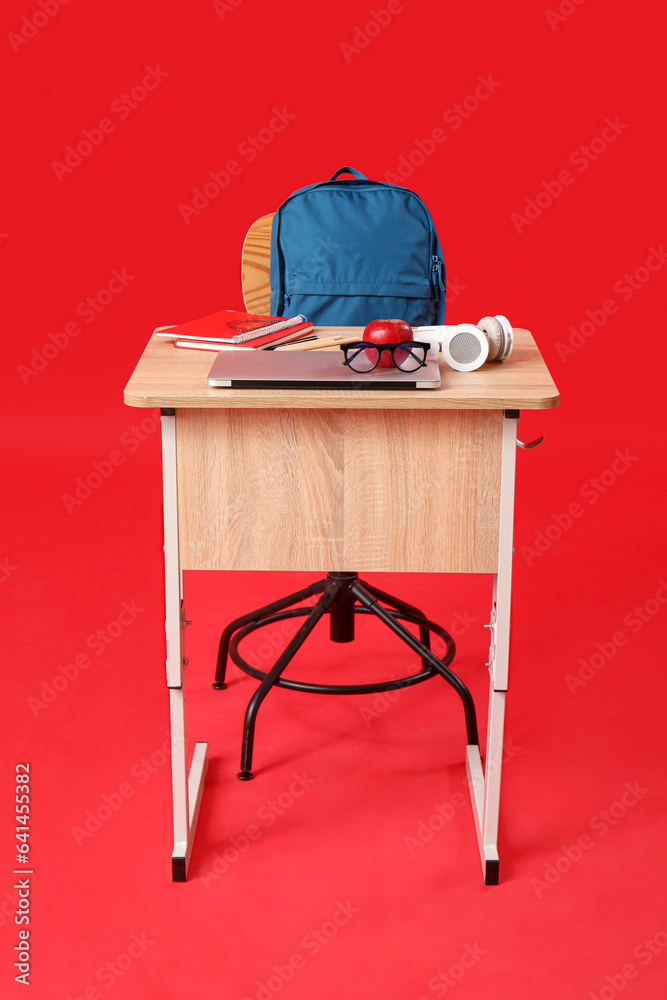 Modern school desk with backpack, gadgets and stationery on red background