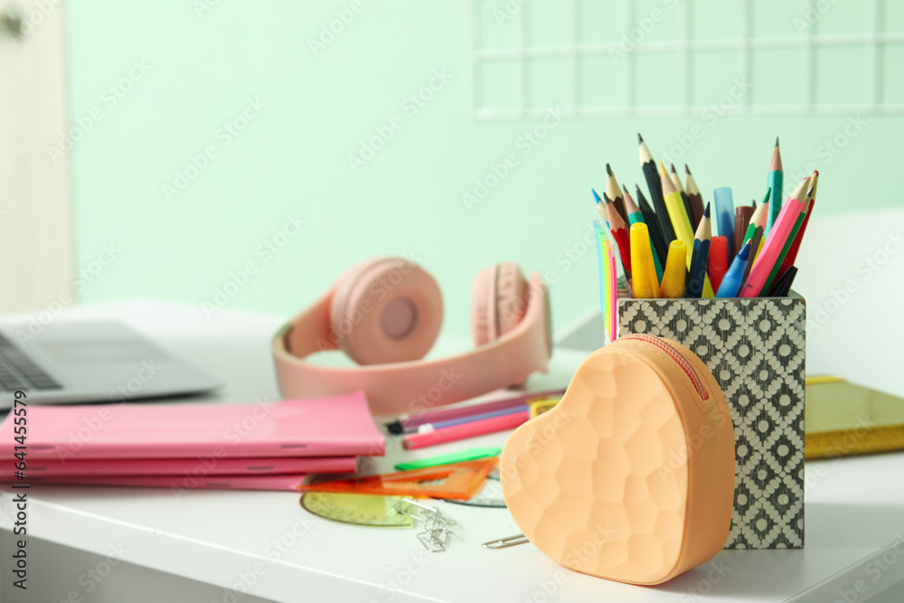 Modern school desk with laptop, headphones and stationery in room near green wall