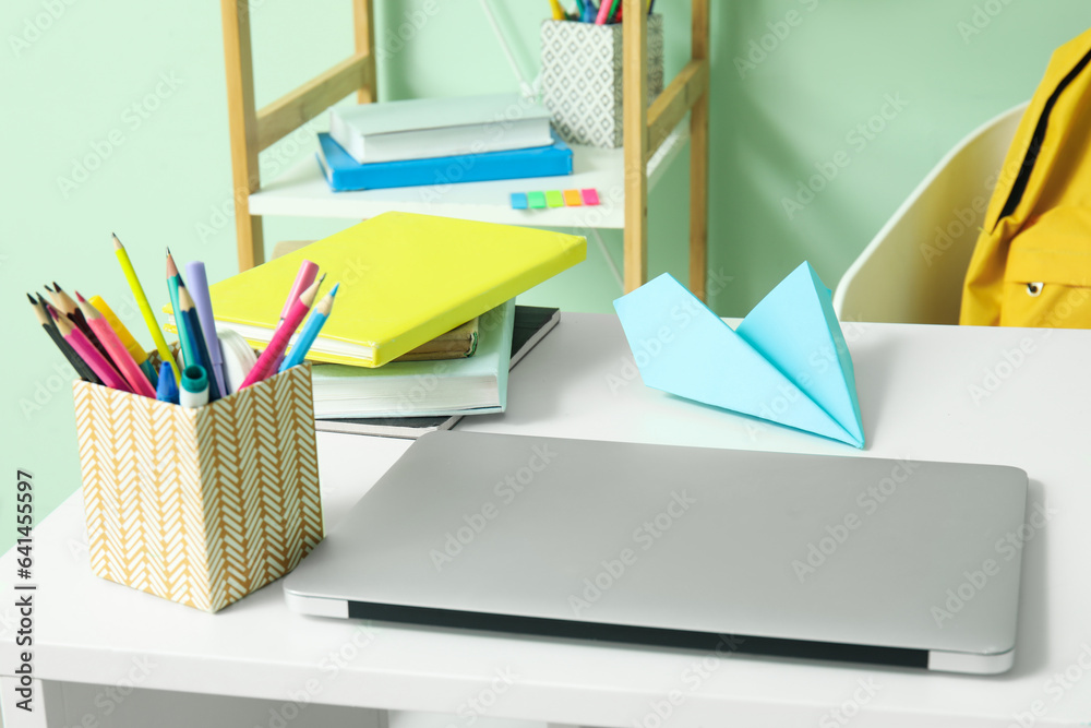 Modern school desk with backpack, laptop and stationery in room near green wall