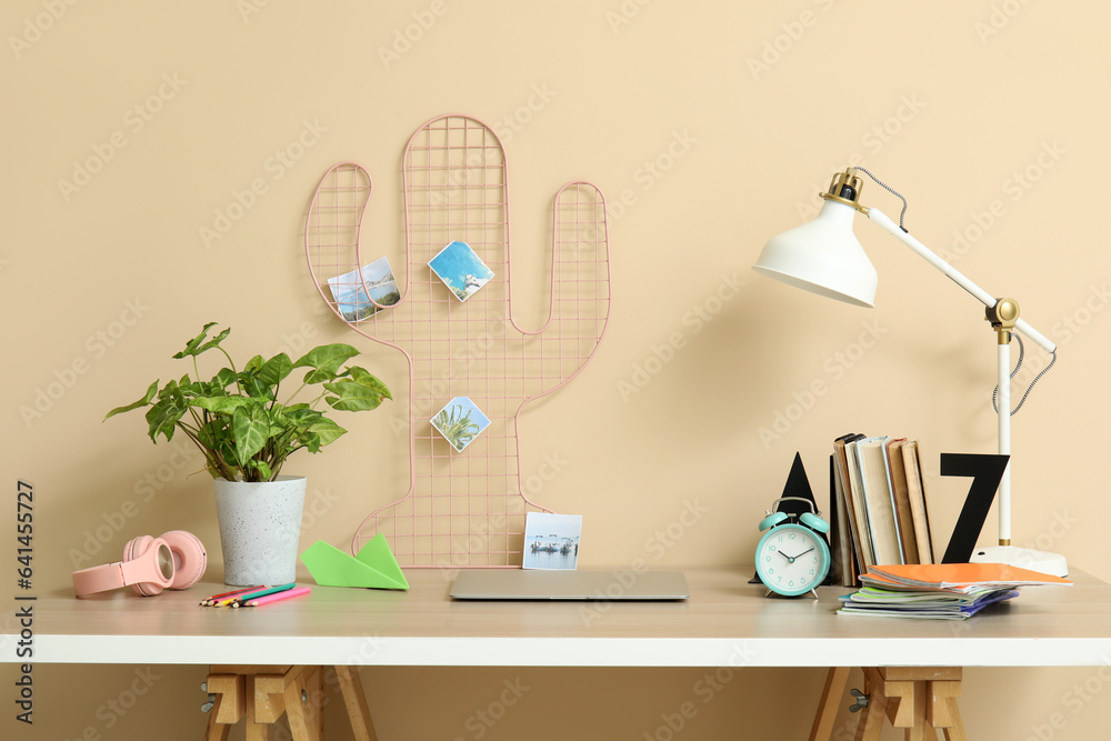 Modern school desk with laptop and stationery in room near beige wall