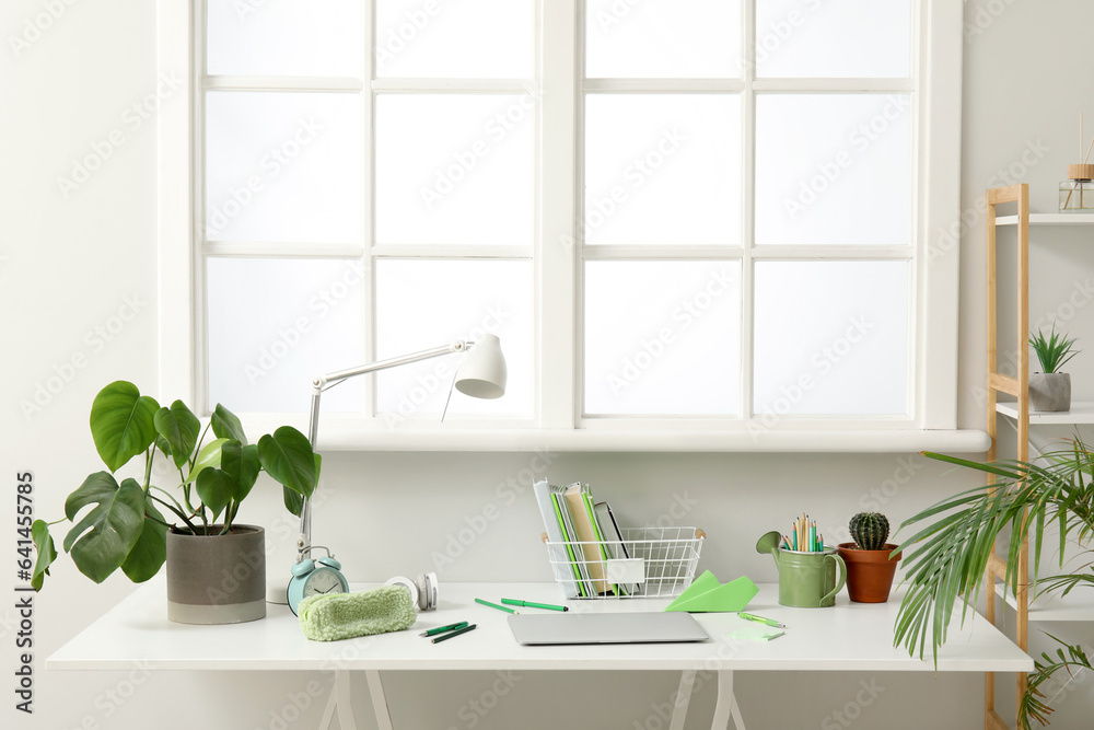 Modern school desk with laptop and stationery in room near white wall