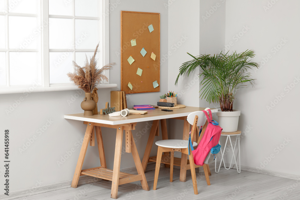 Modern school desk with stationery in room near white wall