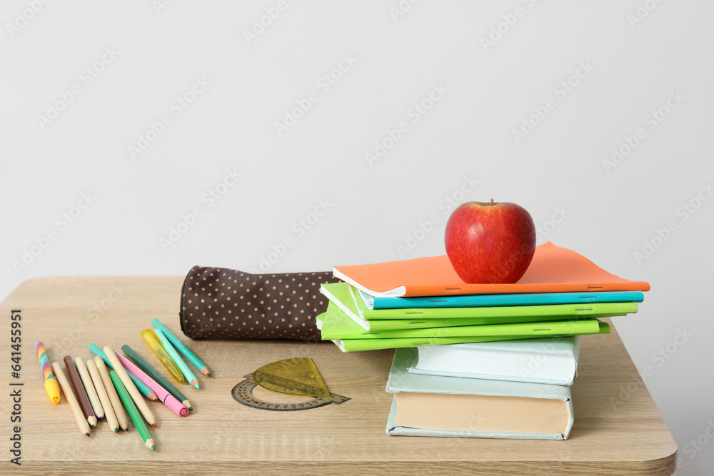 Modern school desk with fresh apple and stationery in room near white wall