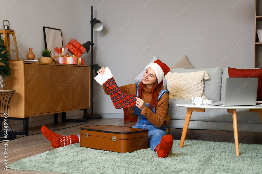 Young woman unpacking suitcase at home on Christmas holidays