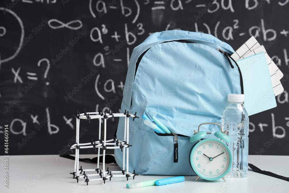 Blue school backpack with stationery, molecular model and bottle of water on white table near black 