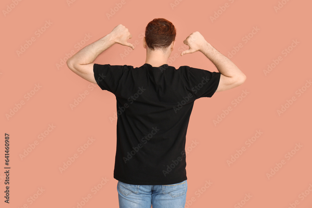 Young man pointing at his black t-shirt on beige background, back view