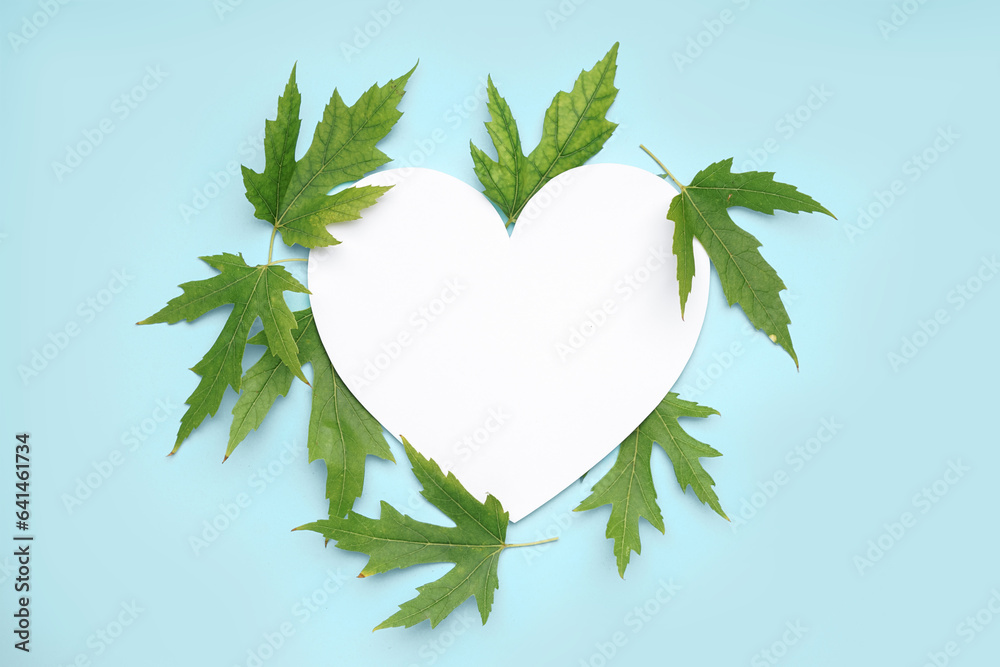 Blank heart shaped card and green leaves on blue background