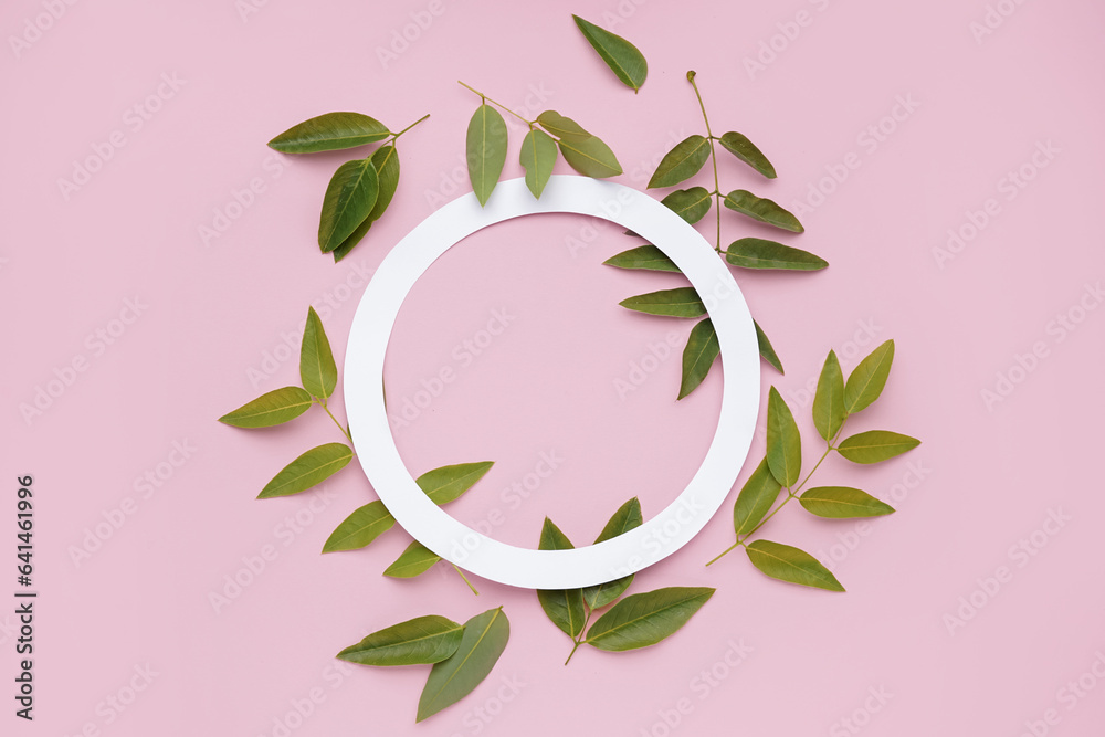 Composition with green leaves and paper circle frame on pink background