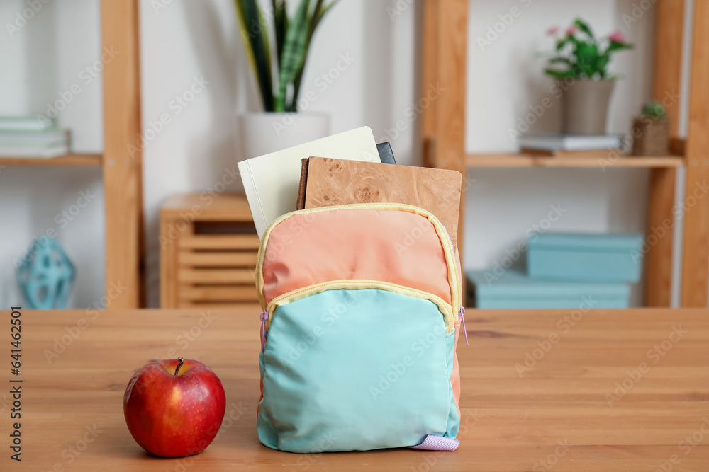 Stylish school backpack with stationery and fresh apple on wooden table in living room