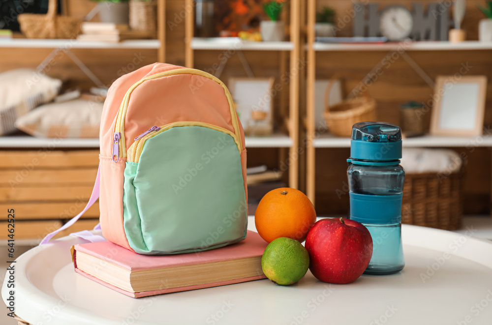 School backpack, bottle of water, book and fruits on table in room