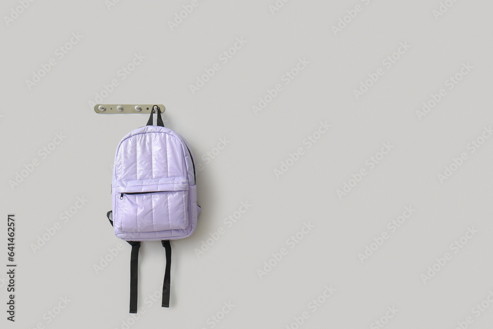 Stylish school backpack hanging on light wall