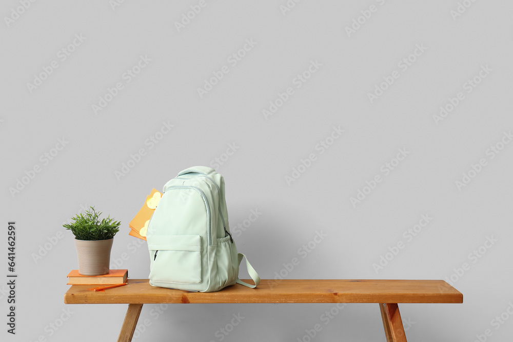 School backpack with stationery and houseplant on wooden table near light wall