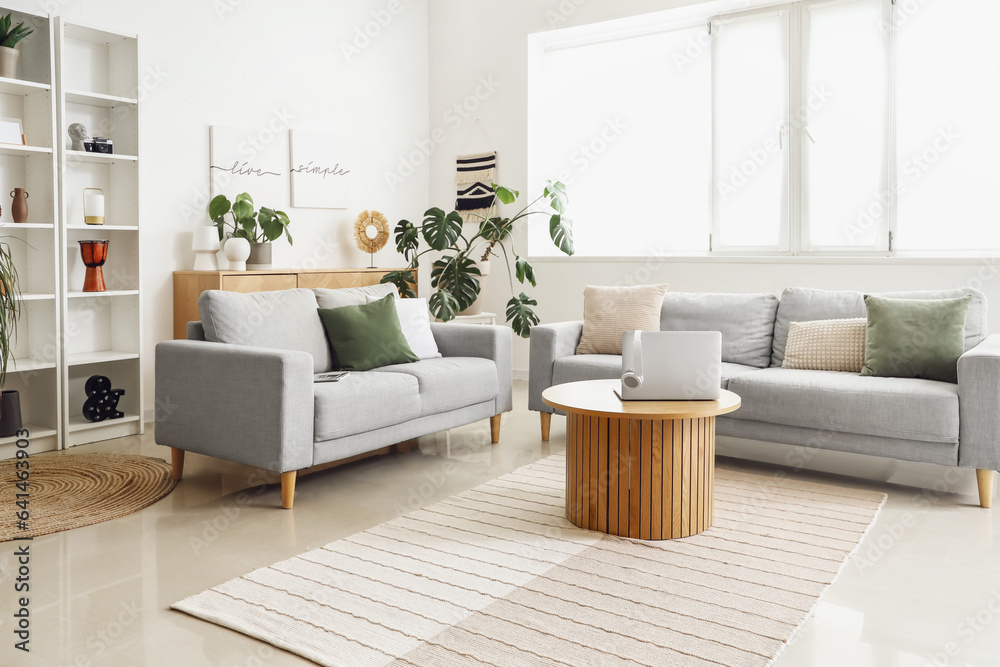 Interior of light living room with sofas and laptop on table