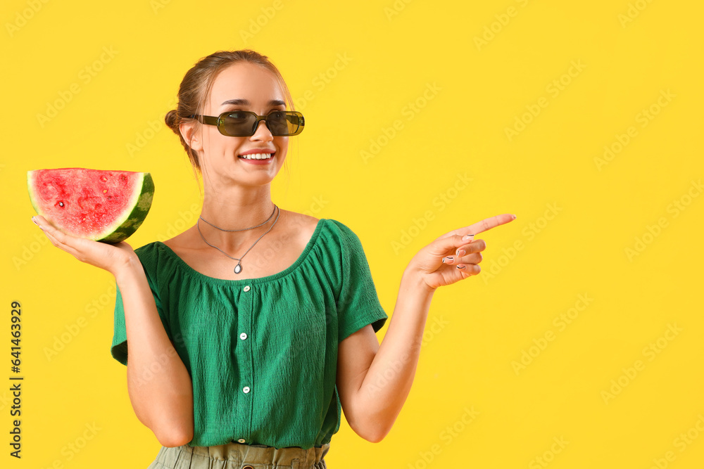 Young woman with fresh watermelon pointing at something on yellow background