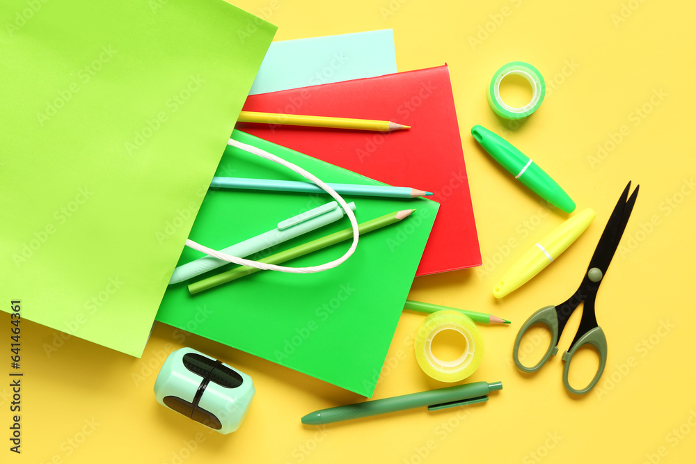 Composition with paper bag with different stationery on yellow background, closeup