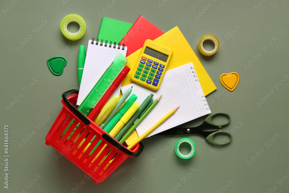 Composition with shopping basket and different stationery on green background