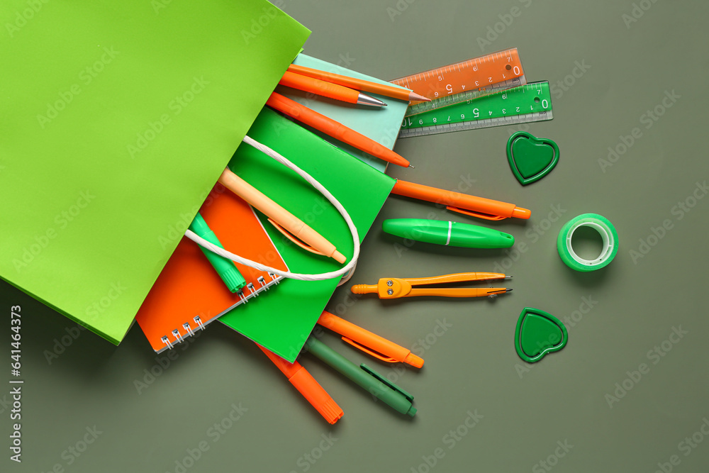 Composition with paper bag with different stationery on color background, closeup