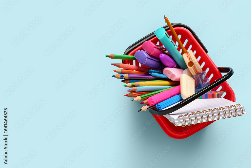 Shopping basket full of different stationery on color background