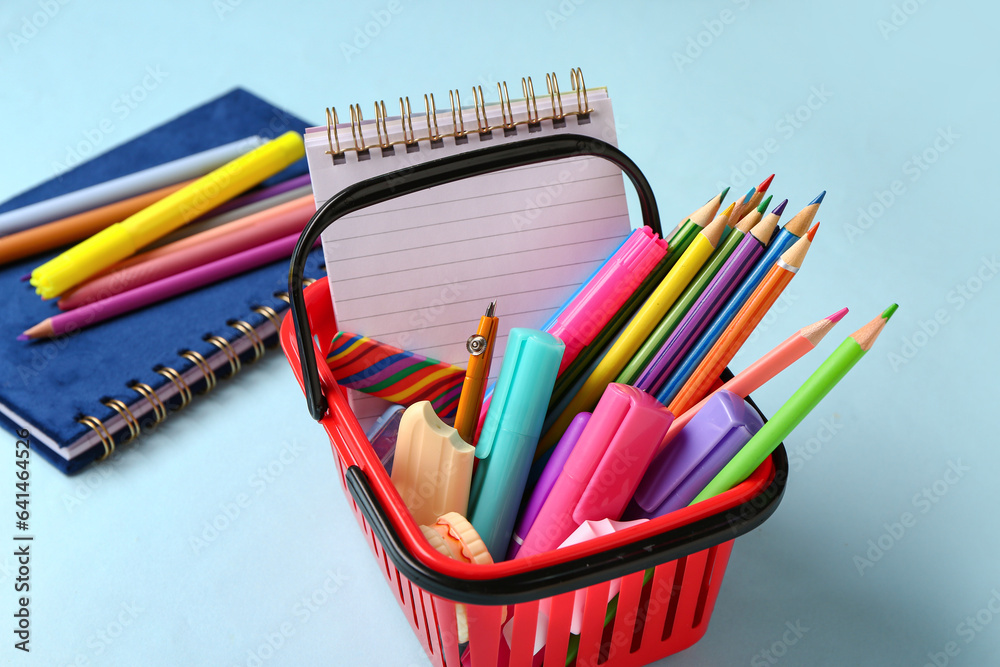 Shopping basket full of different stationery on color background