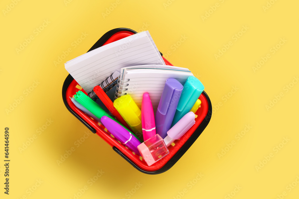 Shopping basket full of stationery on color background