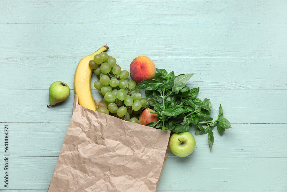 Paper bag full of fresh fruits and herbs on green wooden background