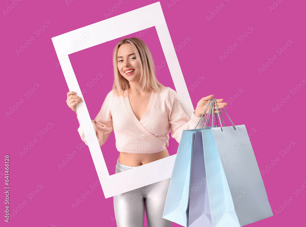 Young beautiful happy woman with frame and shopping bags on purple background