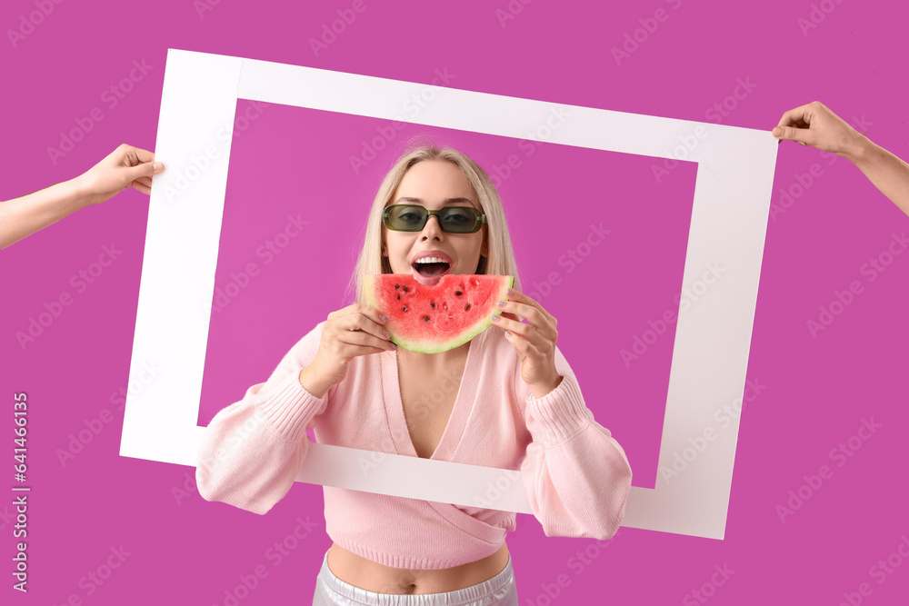 Young beautiful happy woman with slice of fresh watermelon and hands holding frame on purple backgro