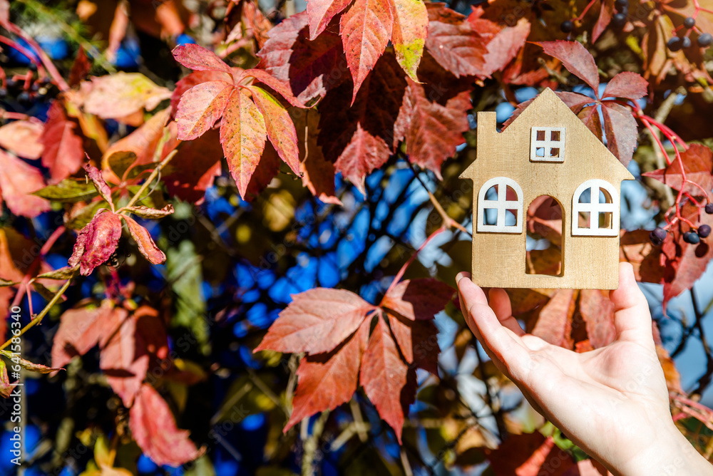 The symbol of the house in the girls hand on the background of red leaves 