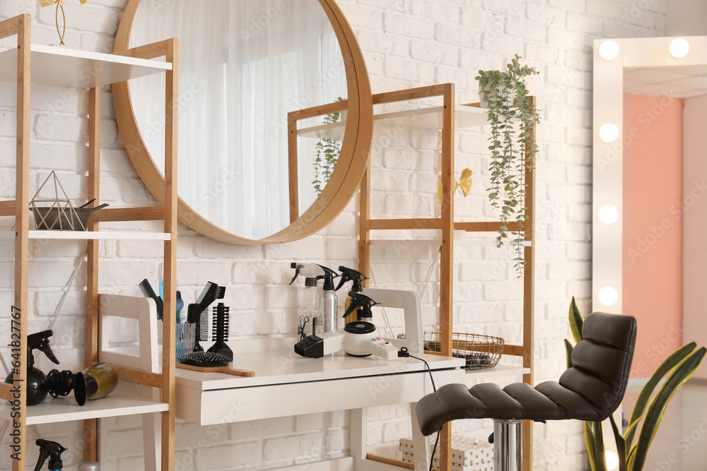 Different hairdressing tools on table near light brick wall in salon