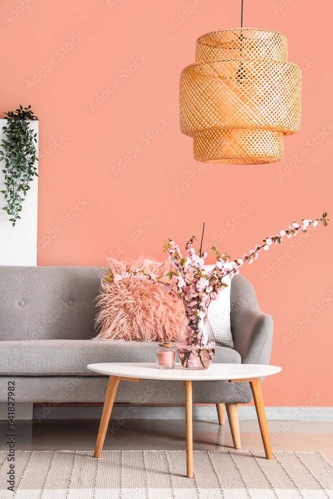 Interior of stylish living room with grey sofa and blooming sakura branches on coffee table