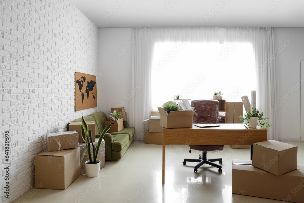 Modern workplace and sofa with cardboard boxes in office on moving day