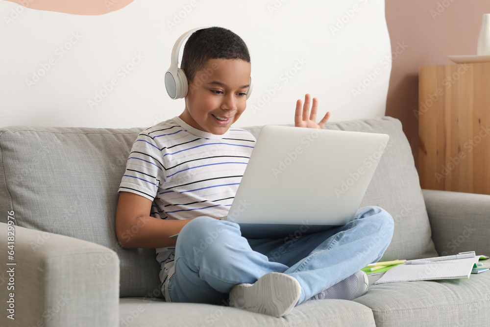 Little African-American boy in headphones with laptop studying computer sciences online at home