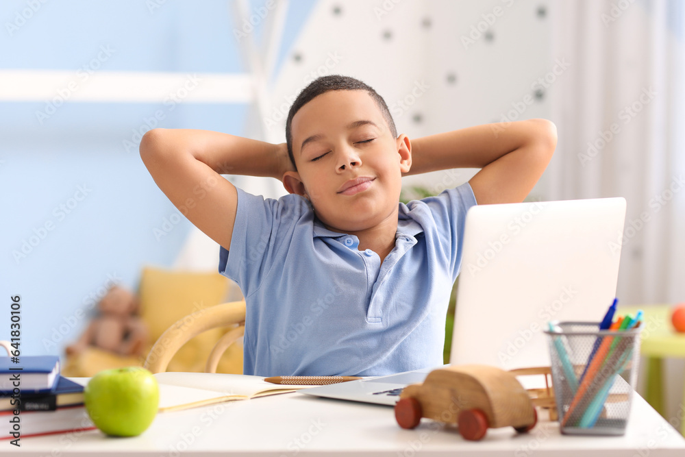 Little African-American boy studying computer sciences online in bedroom